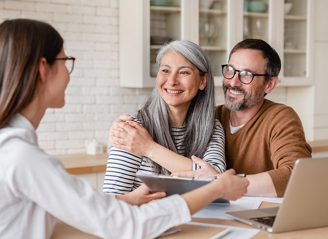 About Our Agency - An Agent Consulting and Showing Contract Documents to a Middle-Aged Couple in Their Home While Smiling