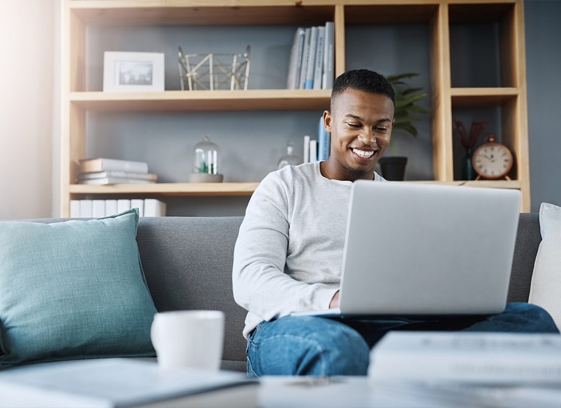 Read Our Reviews - A Shot of a Young Man Using His Laptop While Sitting on a Sofa at Home