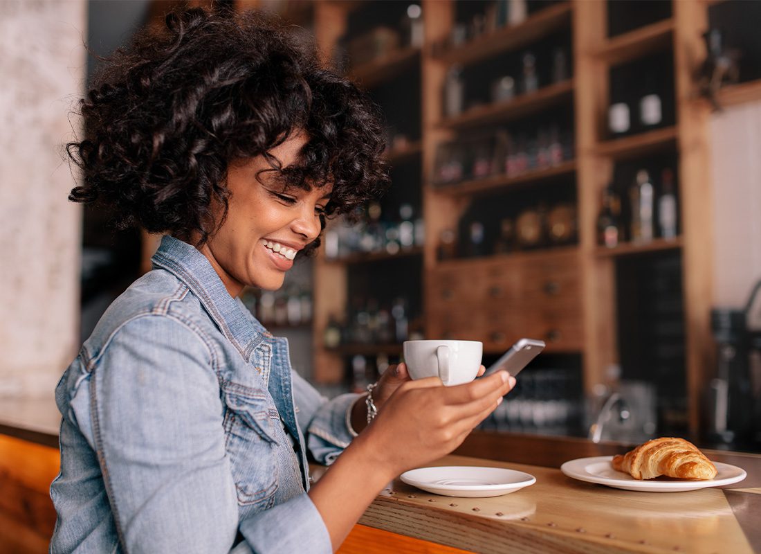Blog - Smiling Woman Using Smart Phone in a Modern Cafe